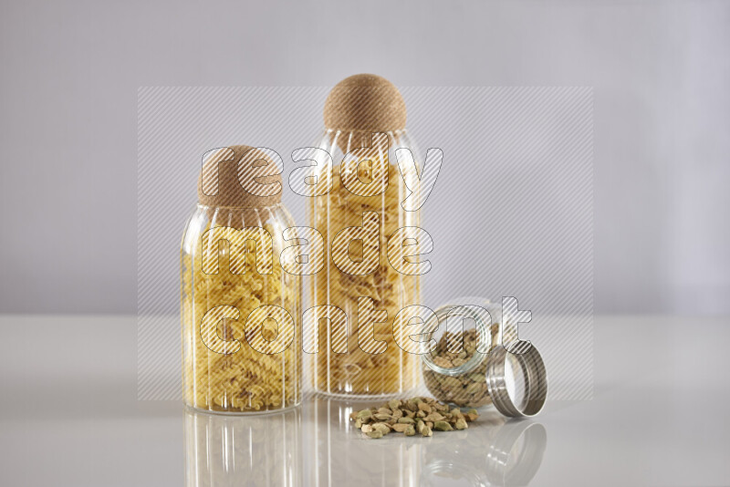 Raw pasta in glass jars with cardamom on light grey background