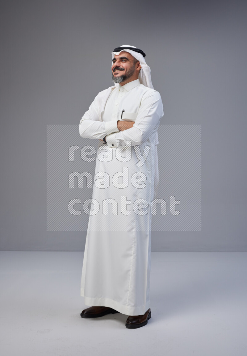 Saudi man Wearing Thob and white Shomag standing with crossed arms on Gray background