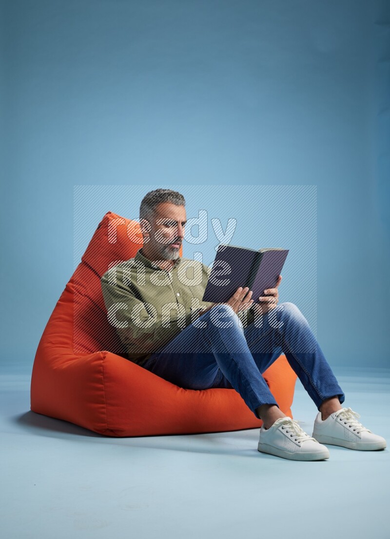A man sitting on an orange beanbag and reading a book