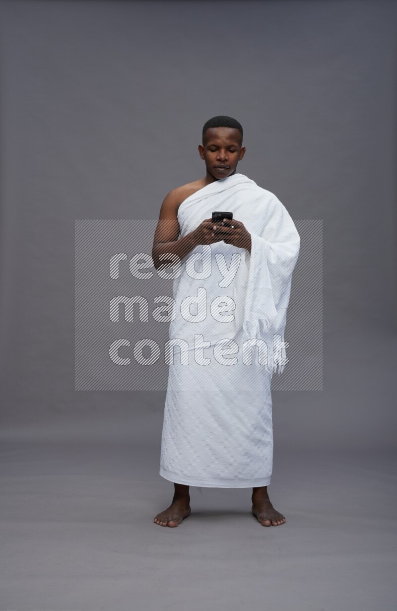 A man wearing Ehram Standing texting on phone on gray background