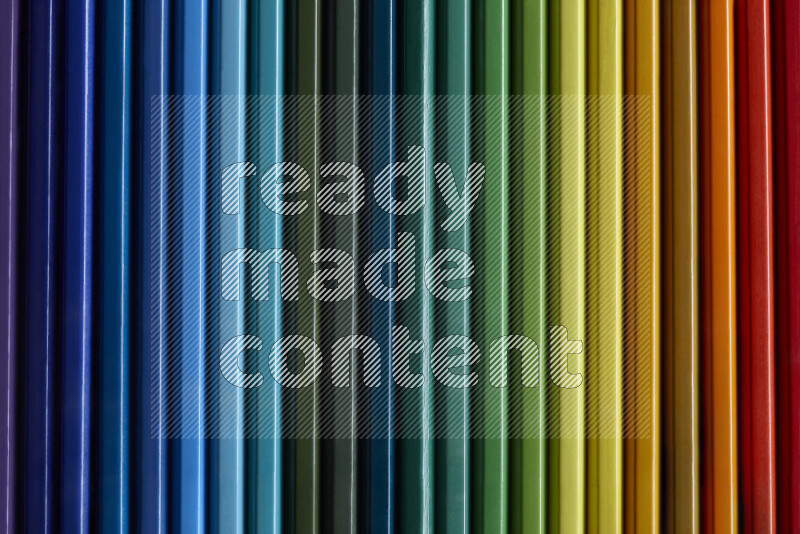 A collection of colored pencils arranged showcasing a gradient of different hues on grey background