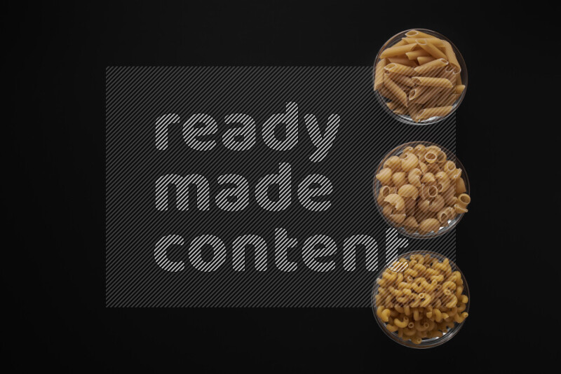 Different pasta types in 3 glass bowls on black background