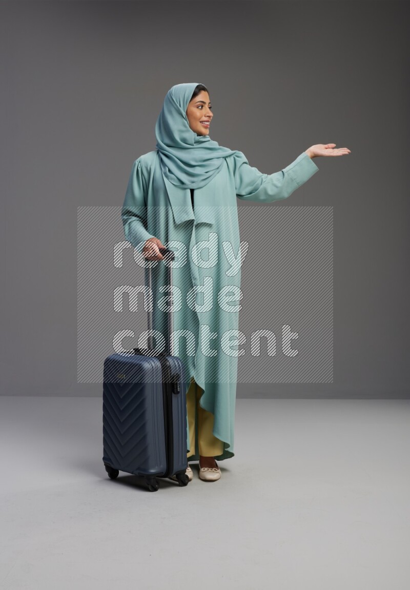 Saudi Woman wearing Abaya standing holding Travel bag on Gray background