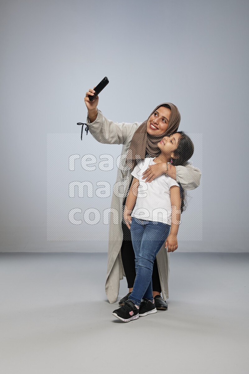 A girl standing taking selfie with her mother on gray background