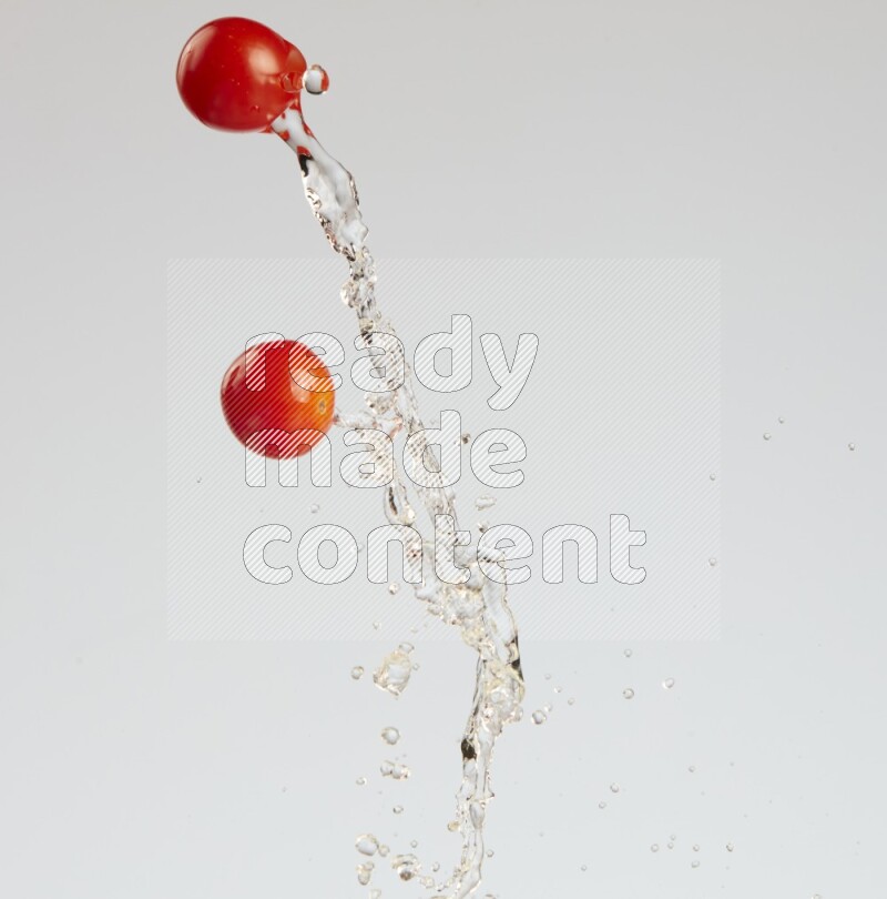 A metal spoon throwing two cherry tomatoes leaving a splash of water behind on a light blue background