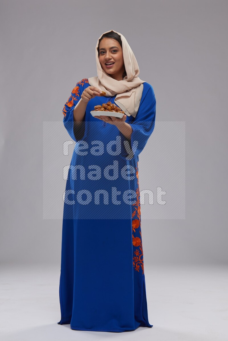 A Saudi woman standing wearing Jalabeya holding a plate of dates