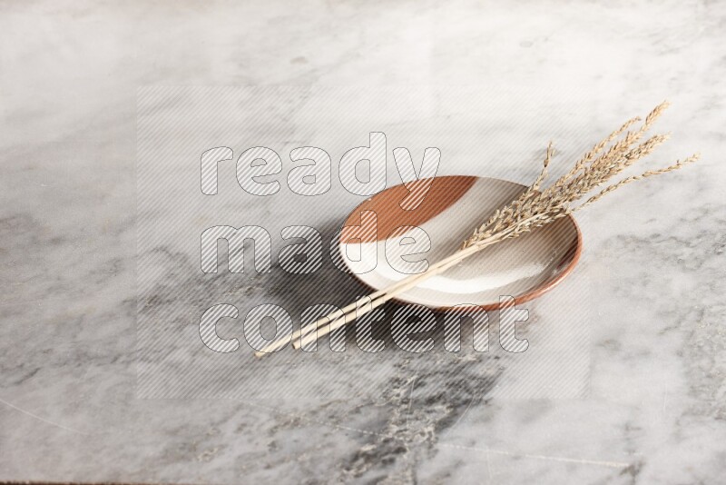 Wheat stalks on multicolored pottery plate on grey marble background