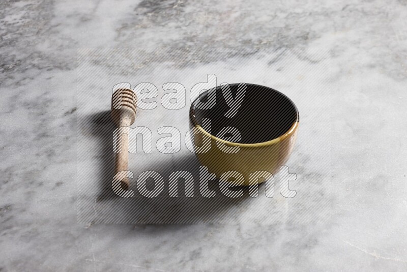 Multicolored pottery bowl with wooden honey dipper on the side on grey marble background
