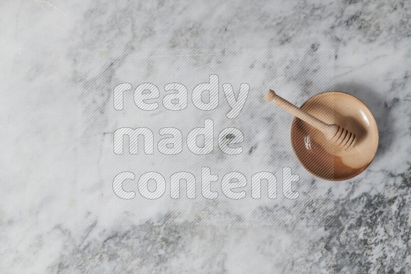 طبق فخاري متعدد الألوان مع ملعقة عسل خشبية بداخله على خلفية من الرخام الرمادي