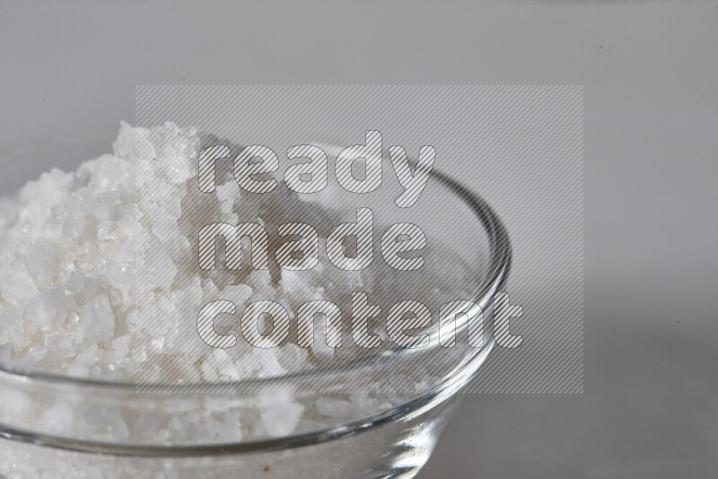 A glass bowl full of coarse sea salt crystals on white background