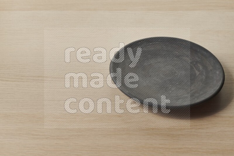 A circular black pottery plate on light wooden background