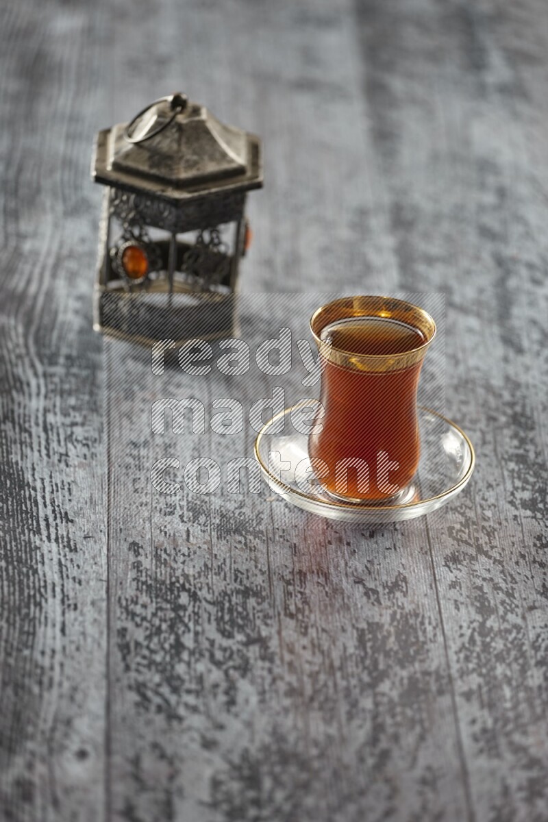 A silver lantern with different drinks, dates, nuts, prayer beads and quran on grey wooden background