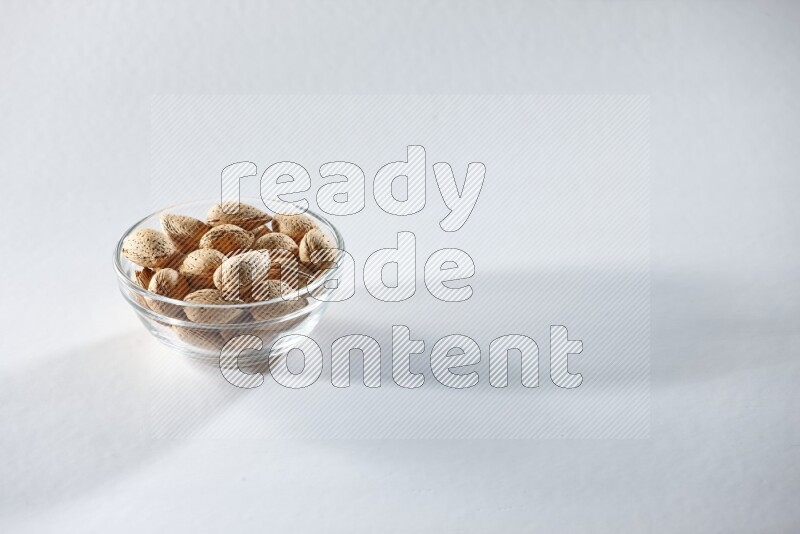 A glass bowl full of almonds on a white background in different angles