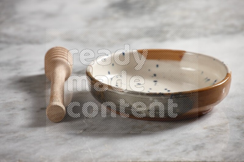 Multicolored pottery bowl with wooden honey dipper on the side on grey marble background