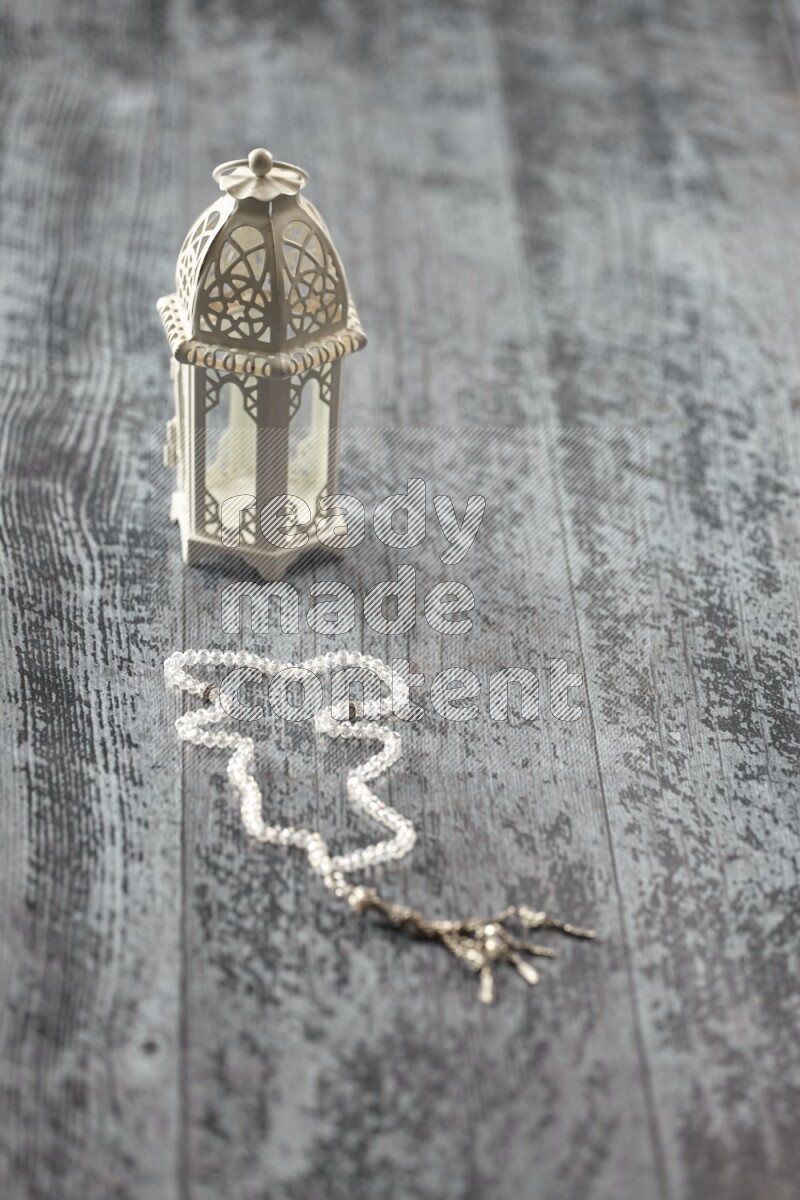 A white lantern with different drinks, dates, nuts, prayer beads and quran on grey wooden background