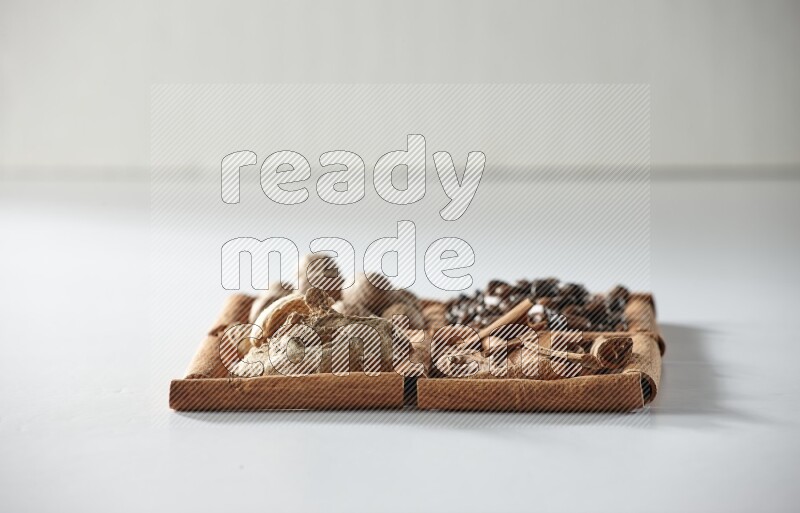 4 مربعات من أعواد القرفة ممتلئة بحبوب القهوة وجوزة الطيب والقرفة والزنجبيل المجفف على أرضية بيضاء