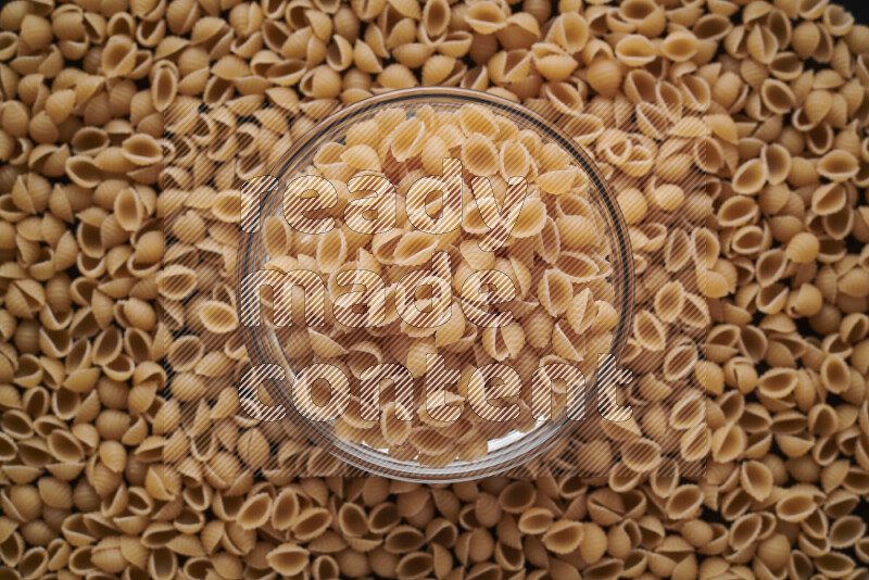 Shells pasta in a glass bowl on black background