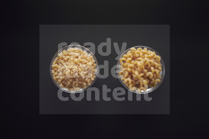 Different pasta types in glass bowls on black background