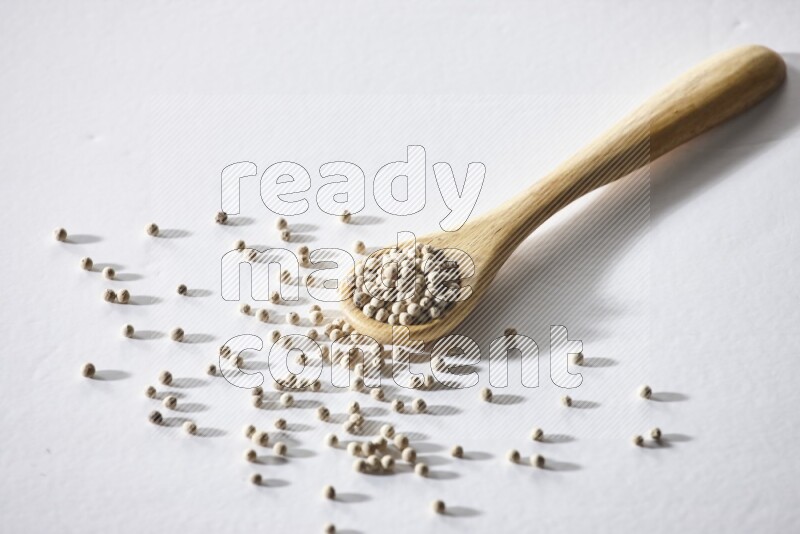 A wooden spoon full of white pepper beads on white flooring