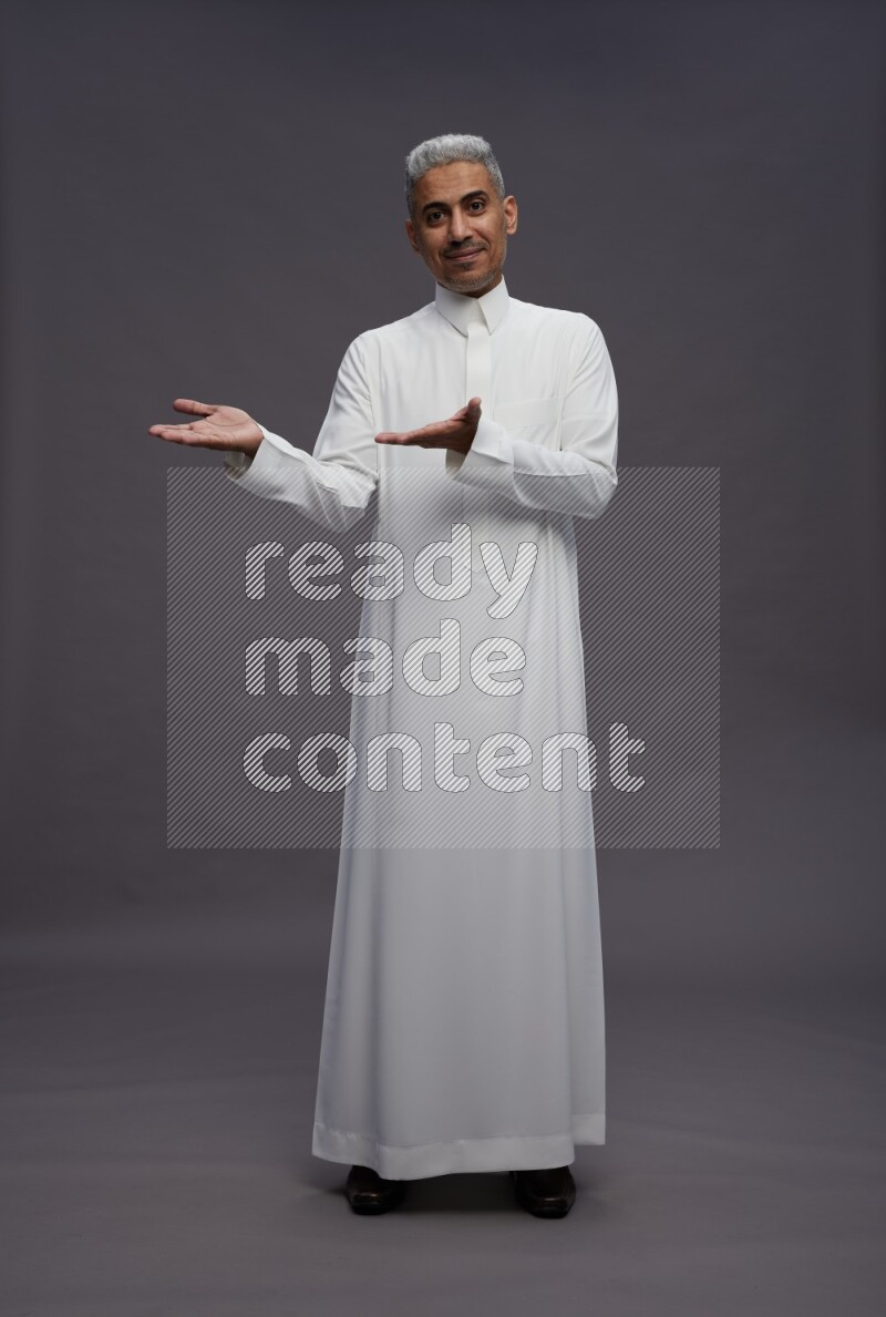 Saudi man wearing thob standing interacting with the camera on gray background