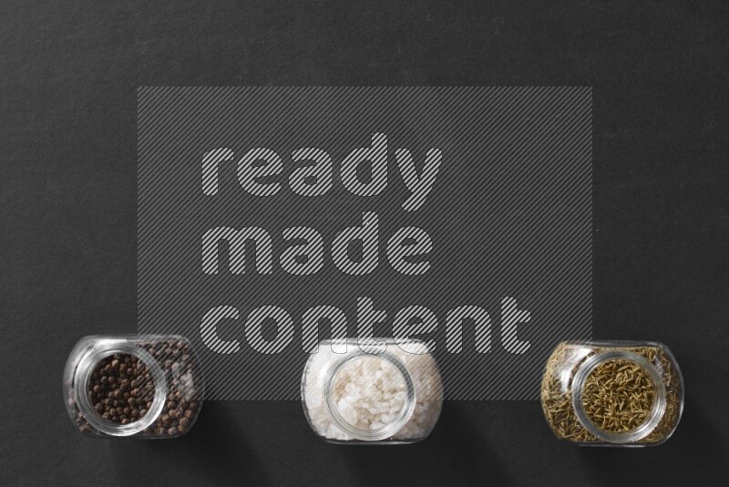 3 glass spice jars full of salt, black peppers and cumin on black flooring