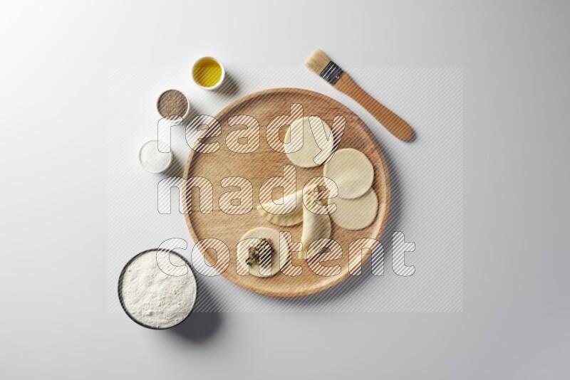 two closed sambosas and one open sambosa filled with meat while flour, salt, black pepper and oil with oil brush aside in a wooden dish on a white background