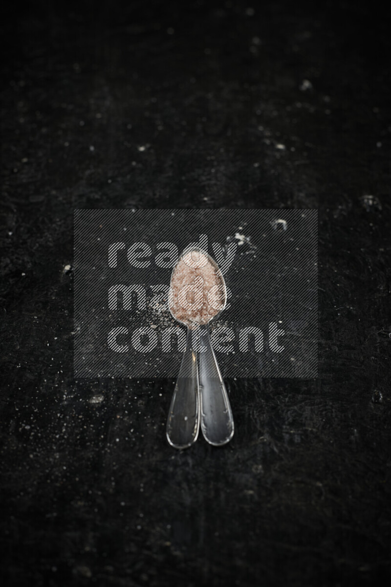 2 metal spoons filled with pink himalayan salt on black background