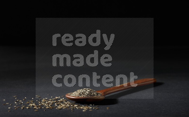 مغرفة خشبية ممتلئة بحبوب الكمون على خلفية سوداء