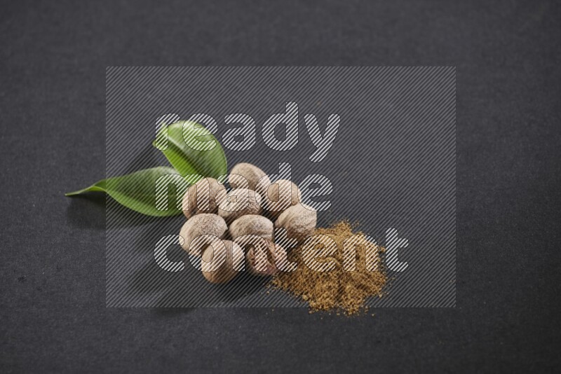 Nutmeg seeds with nutmeg powder beside it on a black flooring in different angles