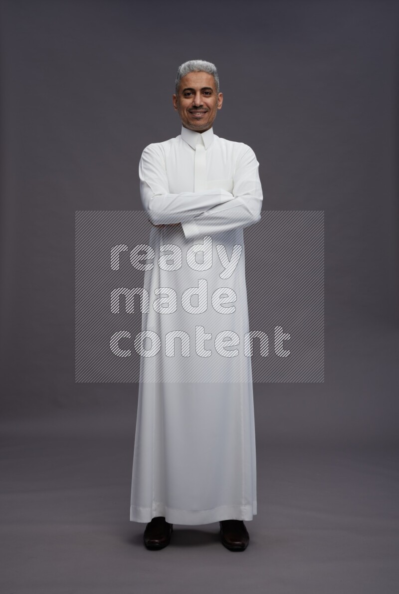 Saudi man wearing thob standing with crossed arms on gray background