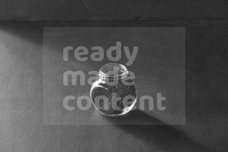 A glass spice jar full of black seeds on black flooring