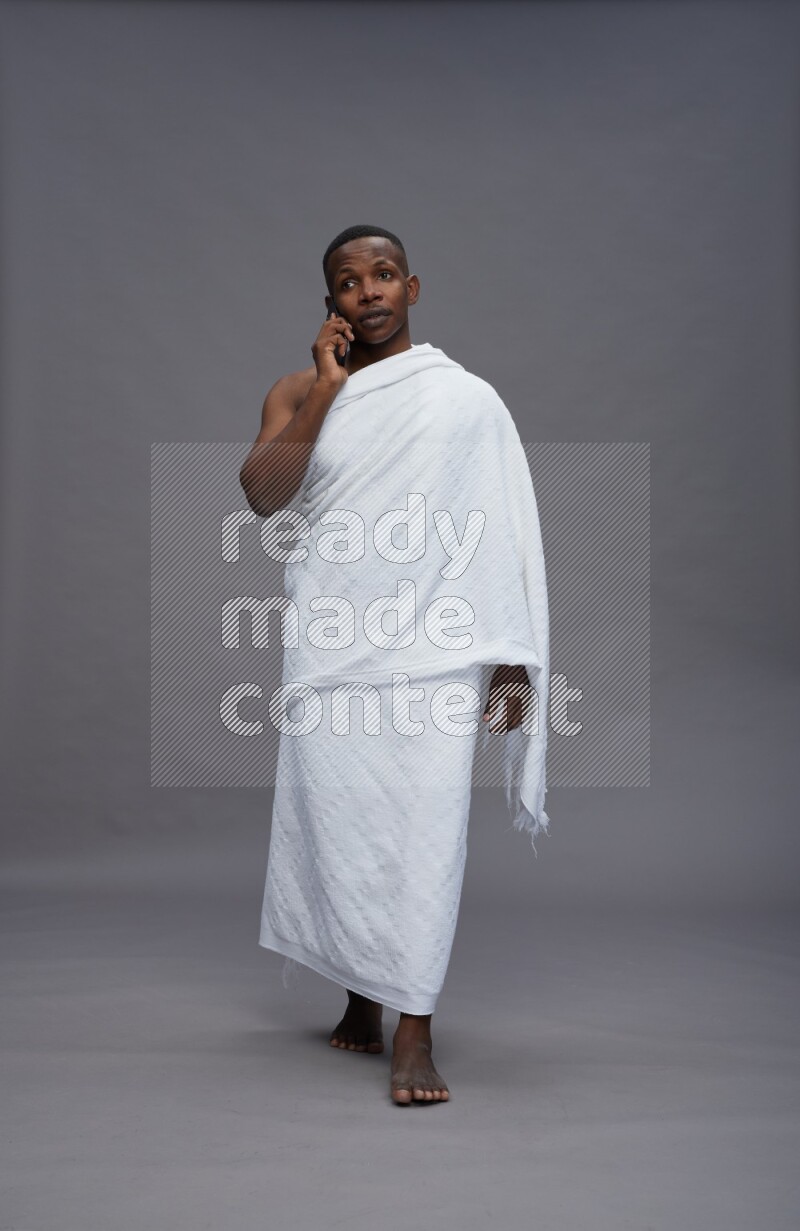 A man wearing Ehram Standing talking on phone on gray background