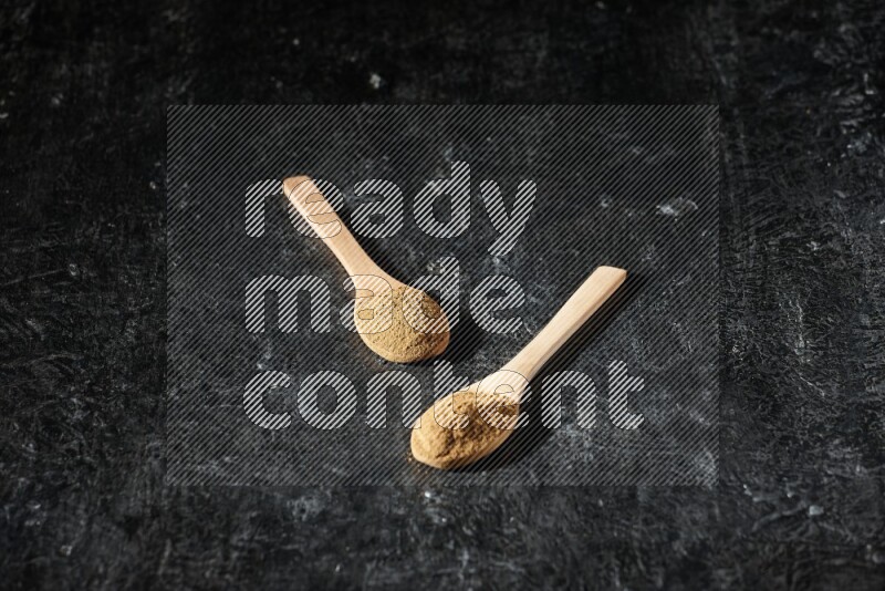 Wooden spoons full of allspice powder on a textured black flooring