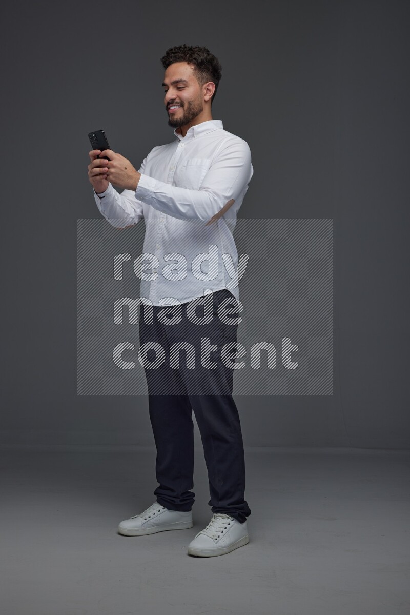 A man wearing smart casual standing and using his phone eye level on a gray background