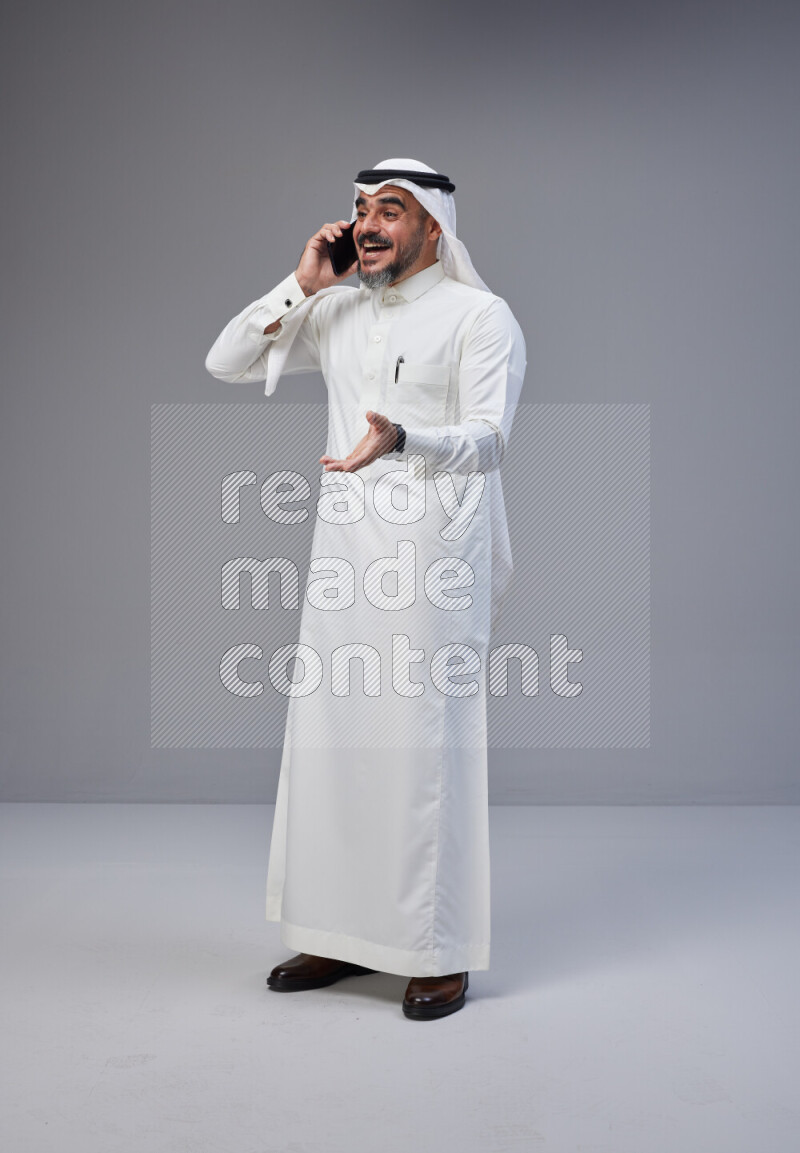 Saudi man Wearing Thob and white Shomag standing talking on phone on Gray background