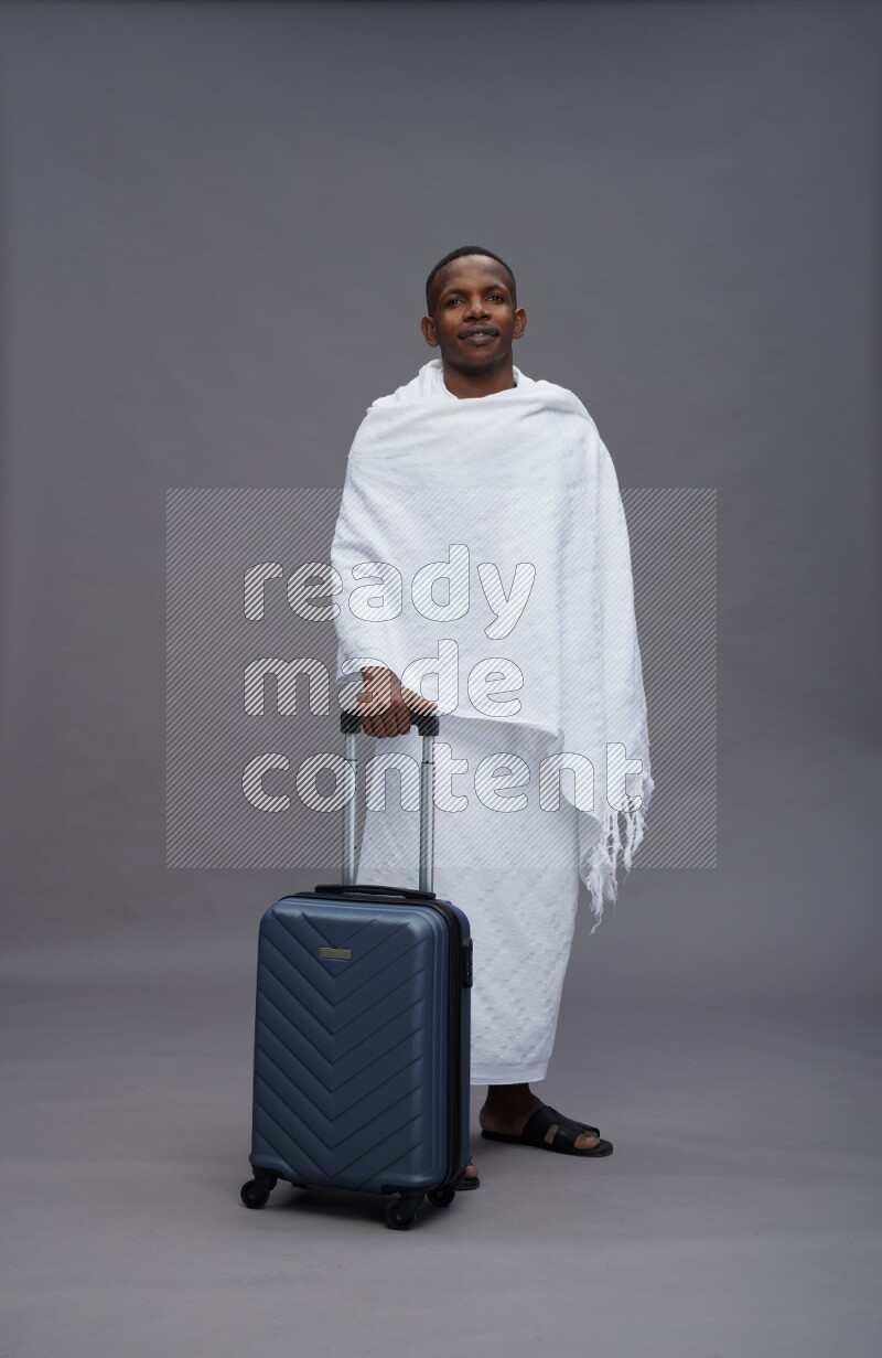 A man wearing Ehram Standing holding traveling bag on gray background