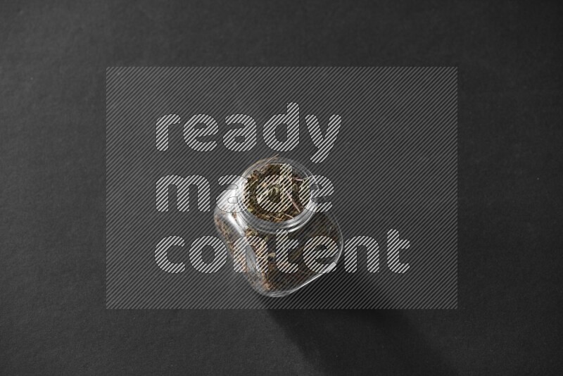 A glass spice jar full of basil on black flooring