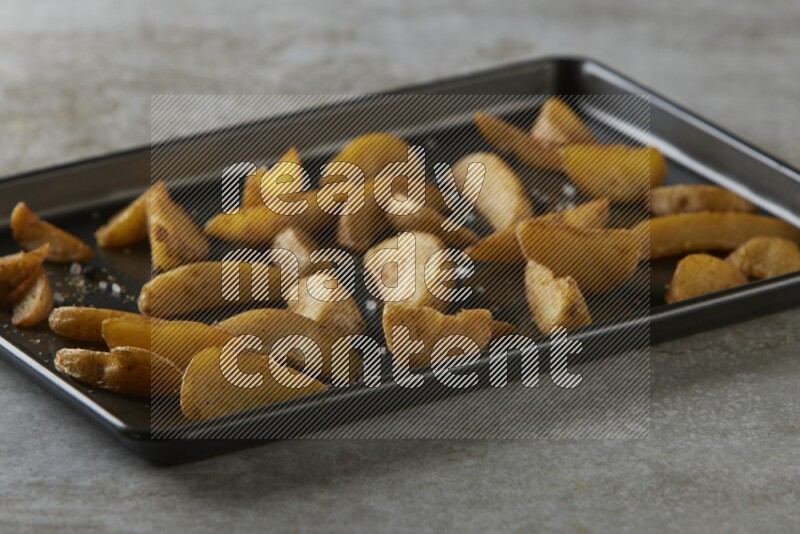 wedges potato in a black stainless steel rectangle tray on grey textured counter top