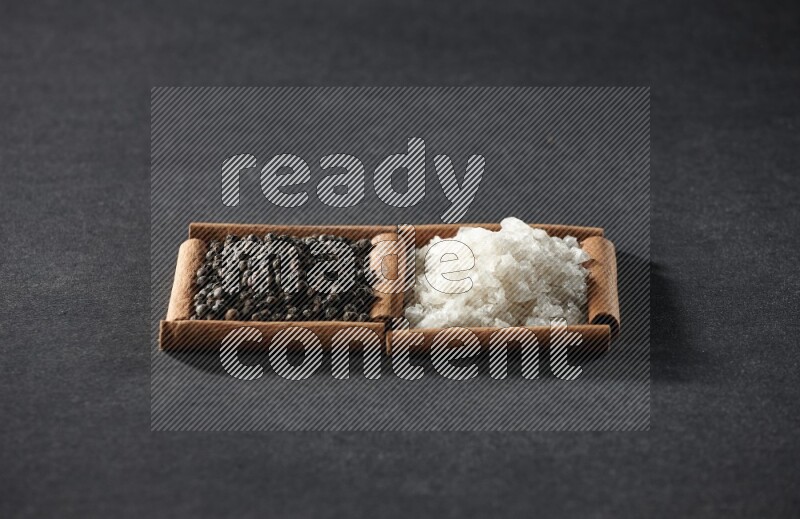 2 squares of cinnamon sticks full of white salt and black peppers on black flooring