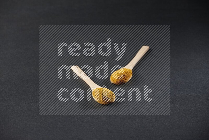 ملعقتان خشبيتان ممتلئتان ببودرة الكركم على خلفية سوداء