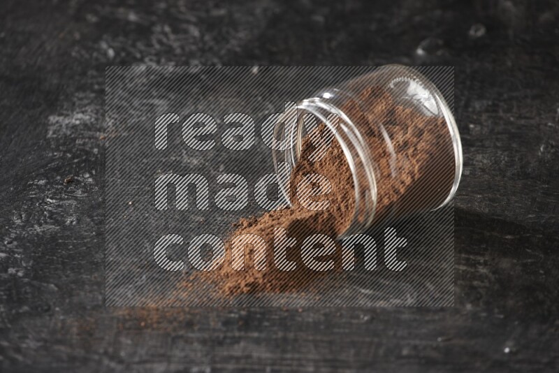 A flipped glass jar full of cloves powder on a textured black flooring