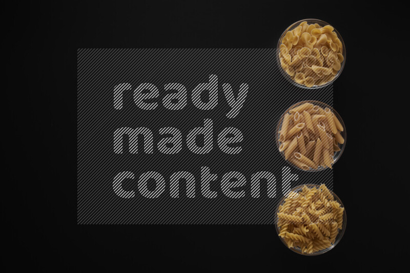 Different pasta types in 3 glass bowls on black background