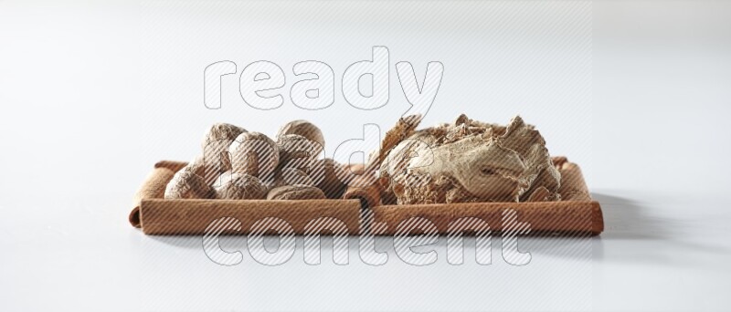 مربعان من أعواد القرفة ممتلئان بالزنجبيل المجفف وجوزة الطيب علي خلفية بيضاء