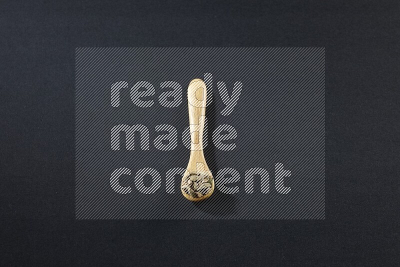 A wooden spoon full of cardamom on black flooring