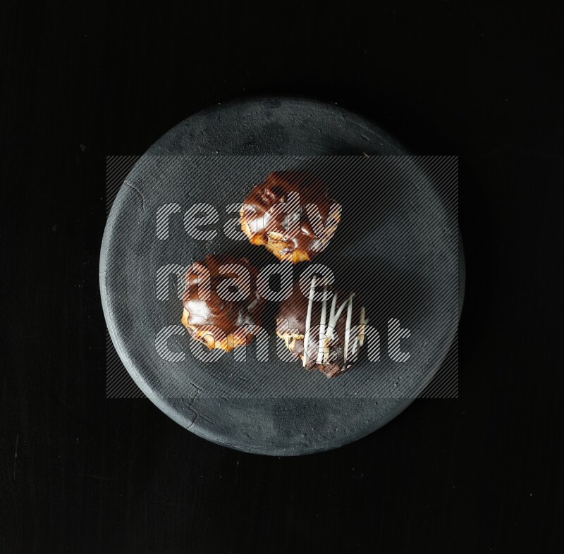 Assorted desserts in a black pottery plate on black background