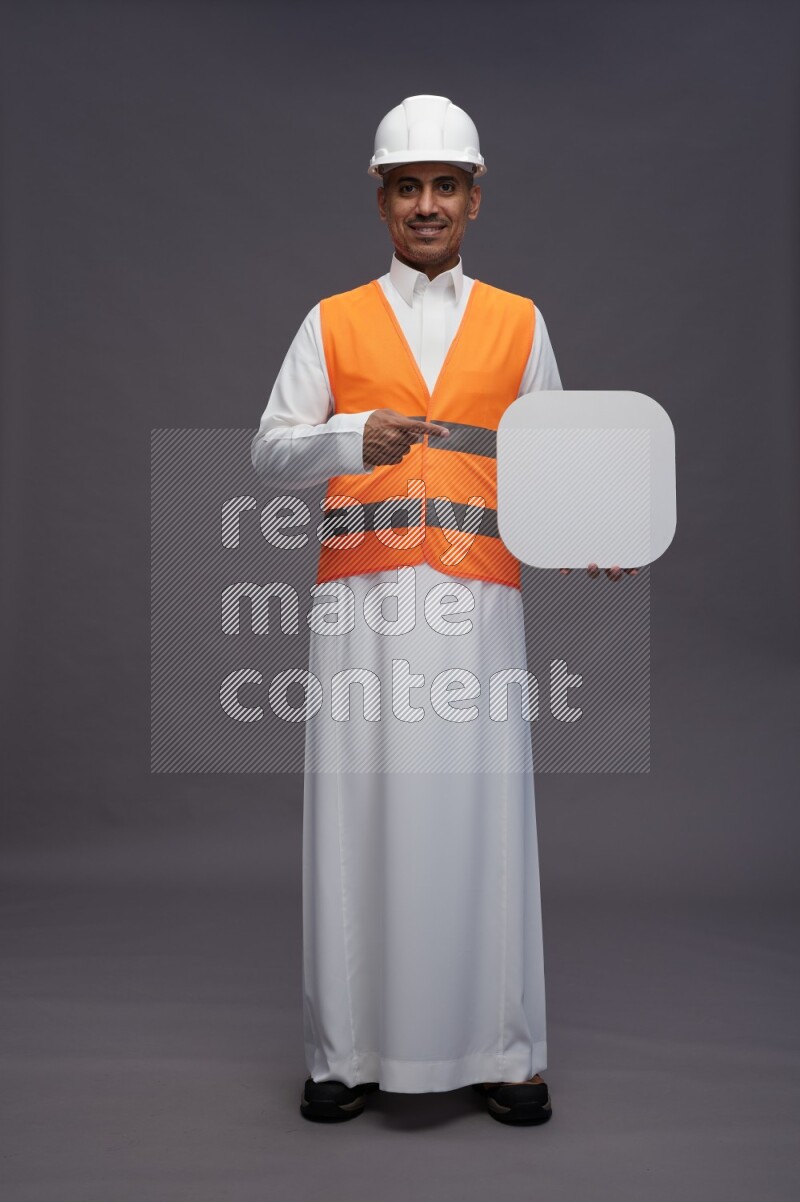Saudi man wearing thob with engineer vest standing holding social media sign on gray background