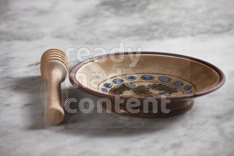 Decorative pottery plate with wooden honey dipper on the side on grey marble background