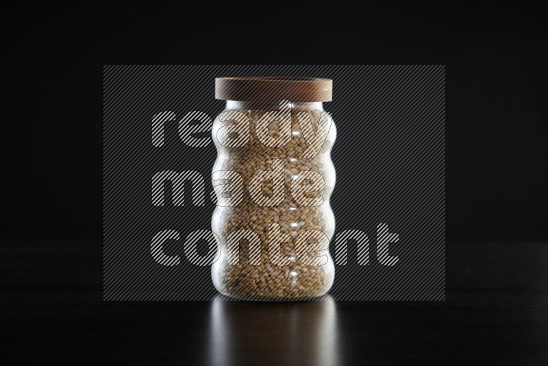 Hulled wheat in a glass jar on black background