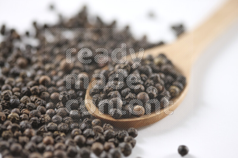 Black pepper beads with wooden spoon on white background