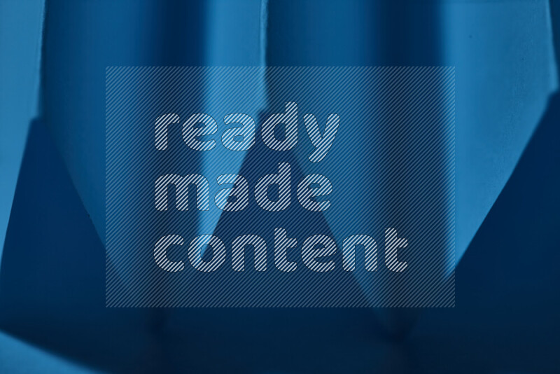 A close-up abstract image showing sharp geometric paper folds in blue gradients